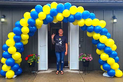 Person standing in doorway under an arch of blue and yellow ballons.