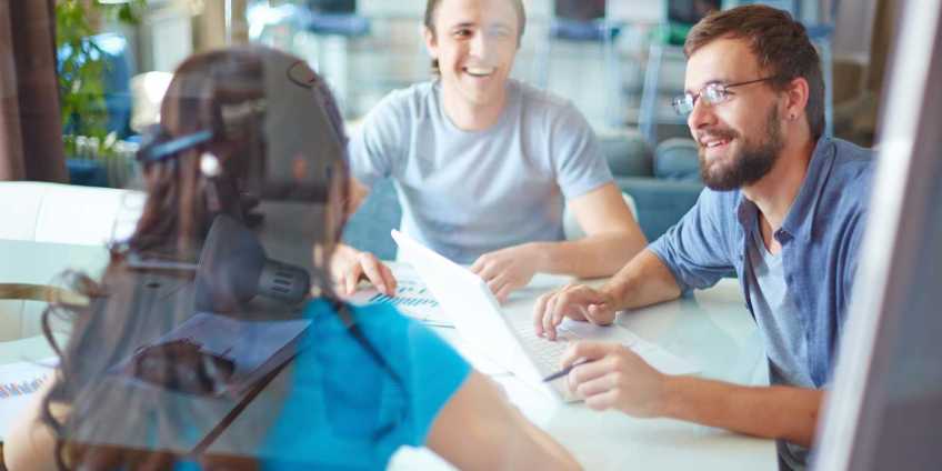 Three young people sitting around a table in a modern open office.