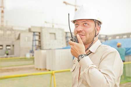 Construction worker wearing a hard hat talking into a radio.