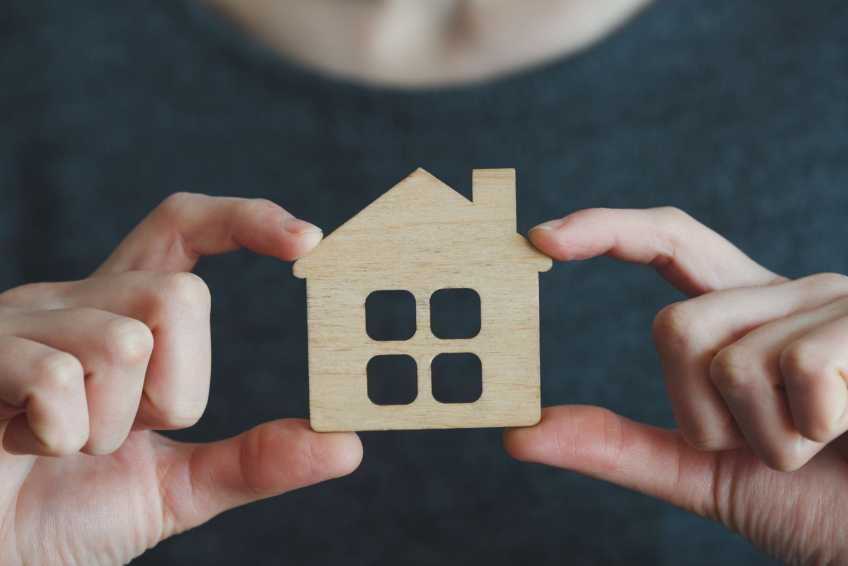 hands holding a piece of cardboard cut to be shaped like a house